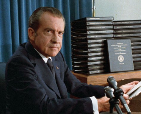 A color photo of President Richard Nixon sitting at desk with microphones